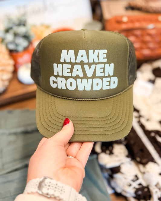 Green cap with 'MAKE HEAVEN CROWDED' text held by a hand against a blurred background