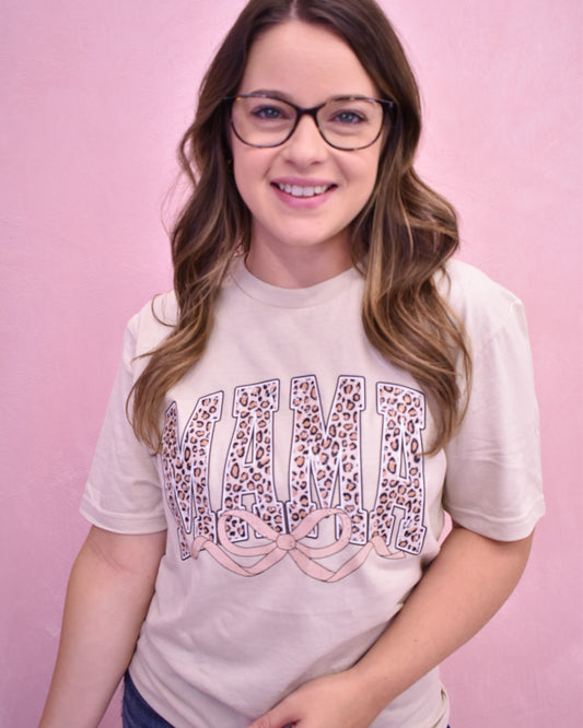 Person wearing a light pink t-shirt with 'Mama' printed on it against a pink background