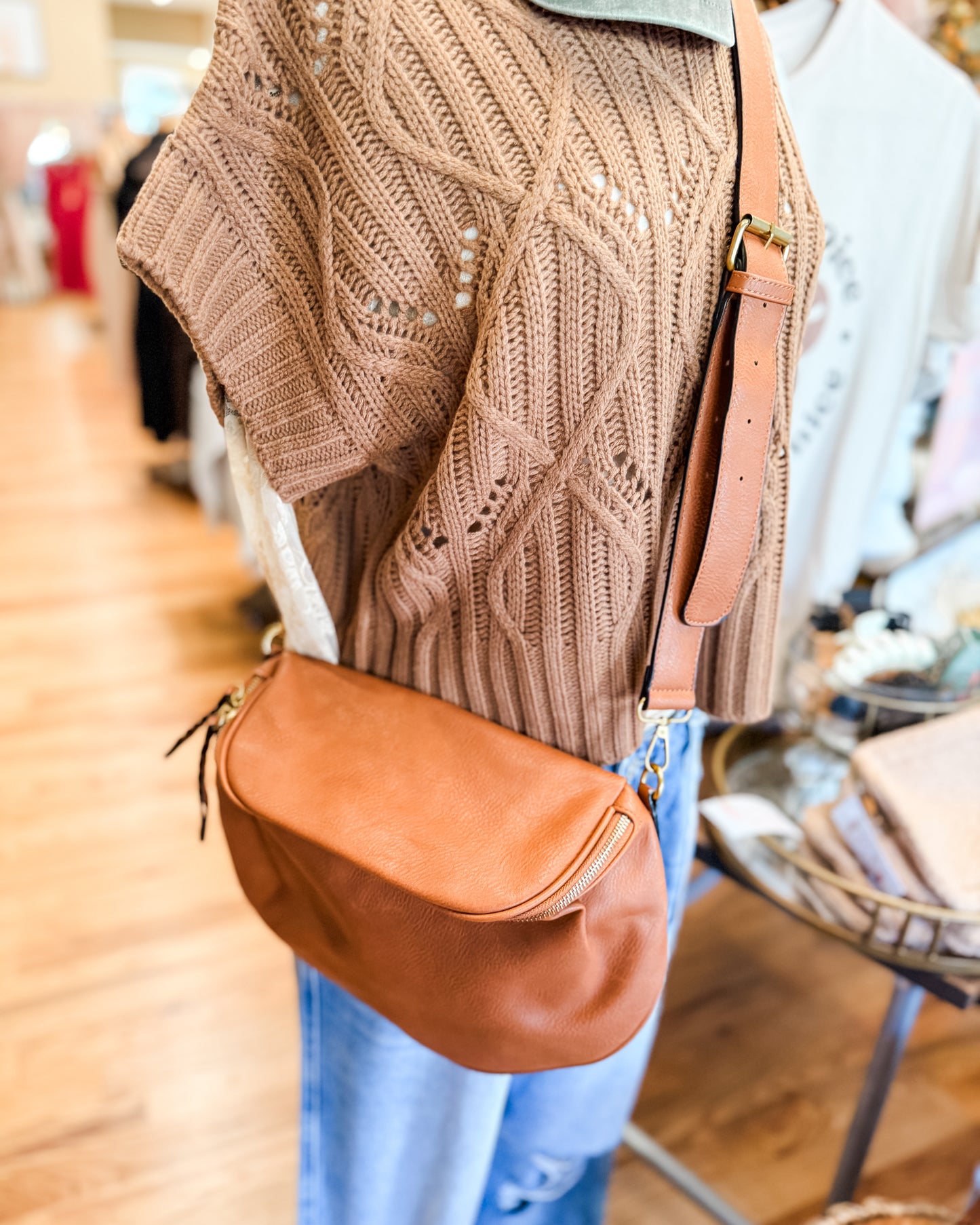 Person wearing a brown knitted sweater and carrying a brown leather bag in a store setting.