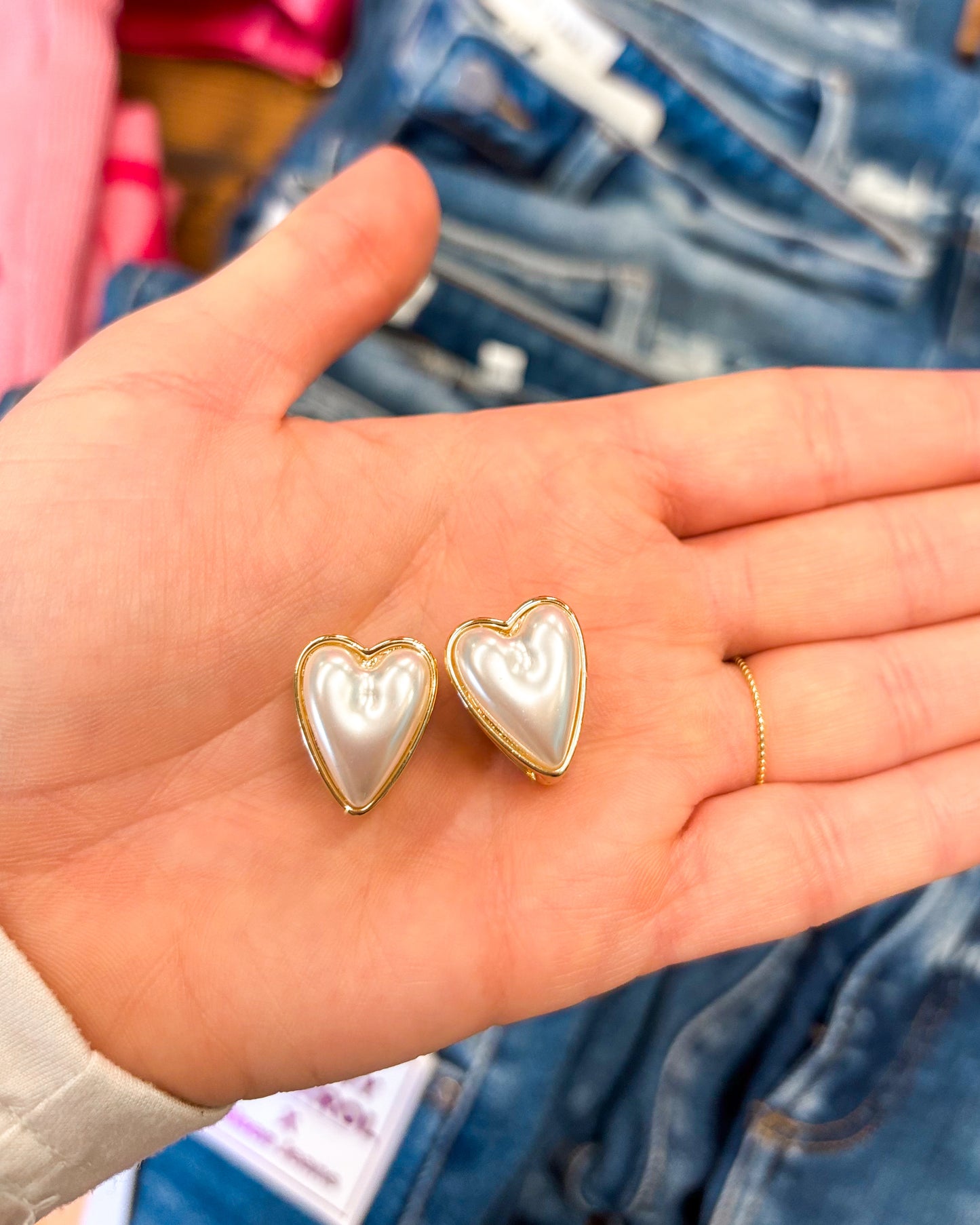 Heart-shaped earrings held in a hand with denim jeans in the background