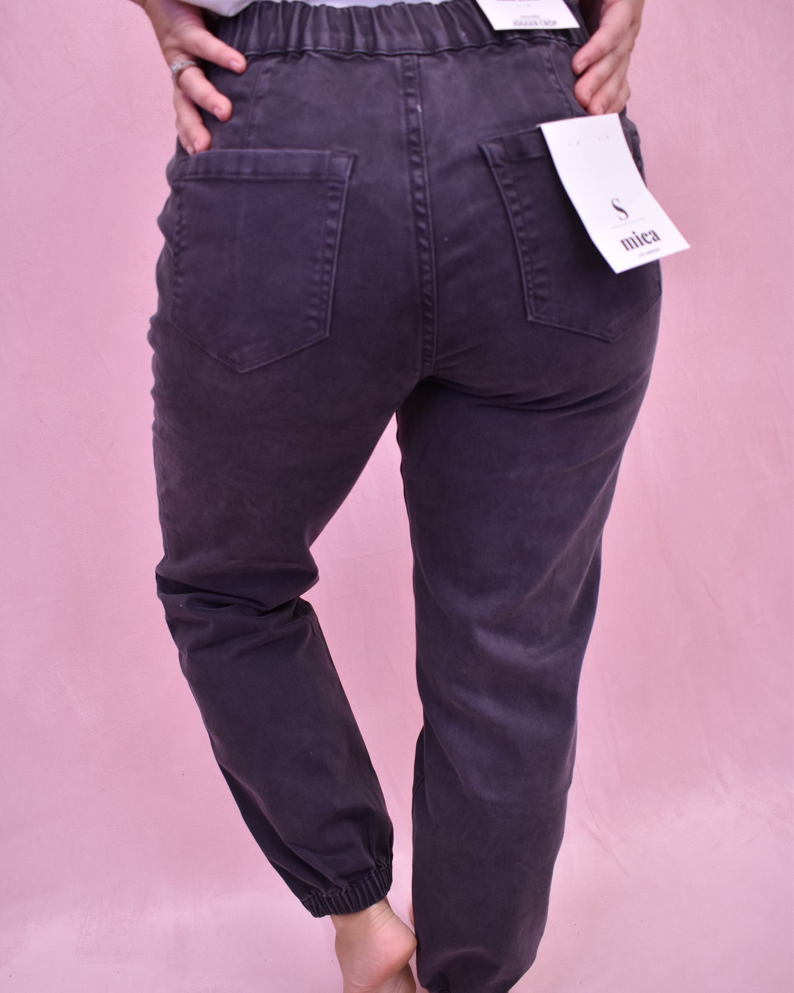 Dark purple jogger pants with a brand tag on a pink background