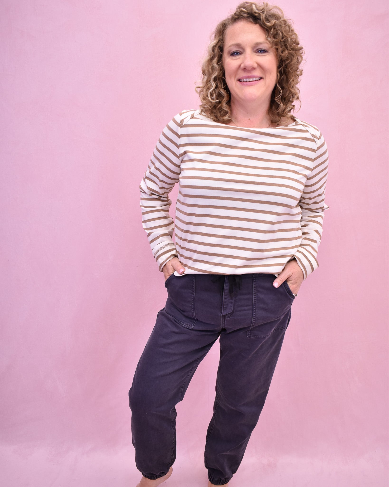 Woman wearing a striped sweater and dark pants against a pink background