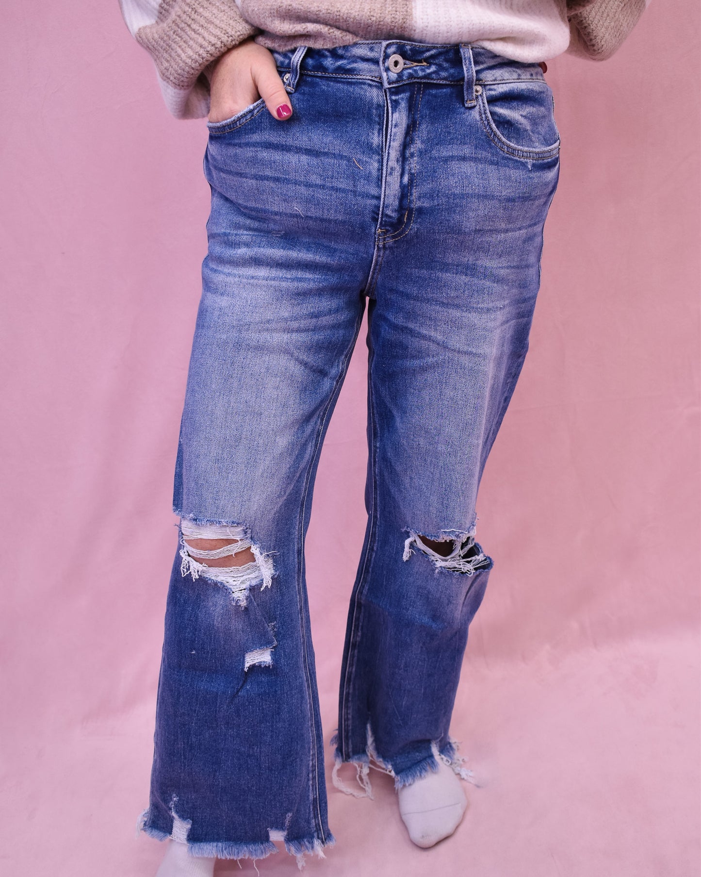 Person wearing blue flared jeans with a pink background