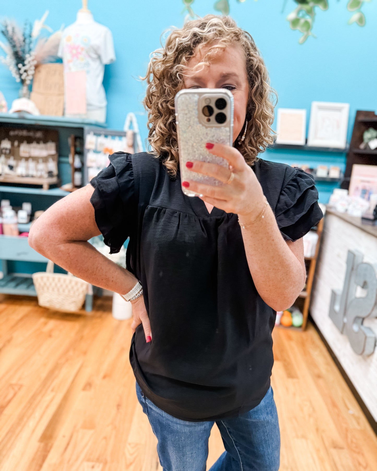 Person taking a mirror selfie wearing a black top and blue jeans in a store setting.