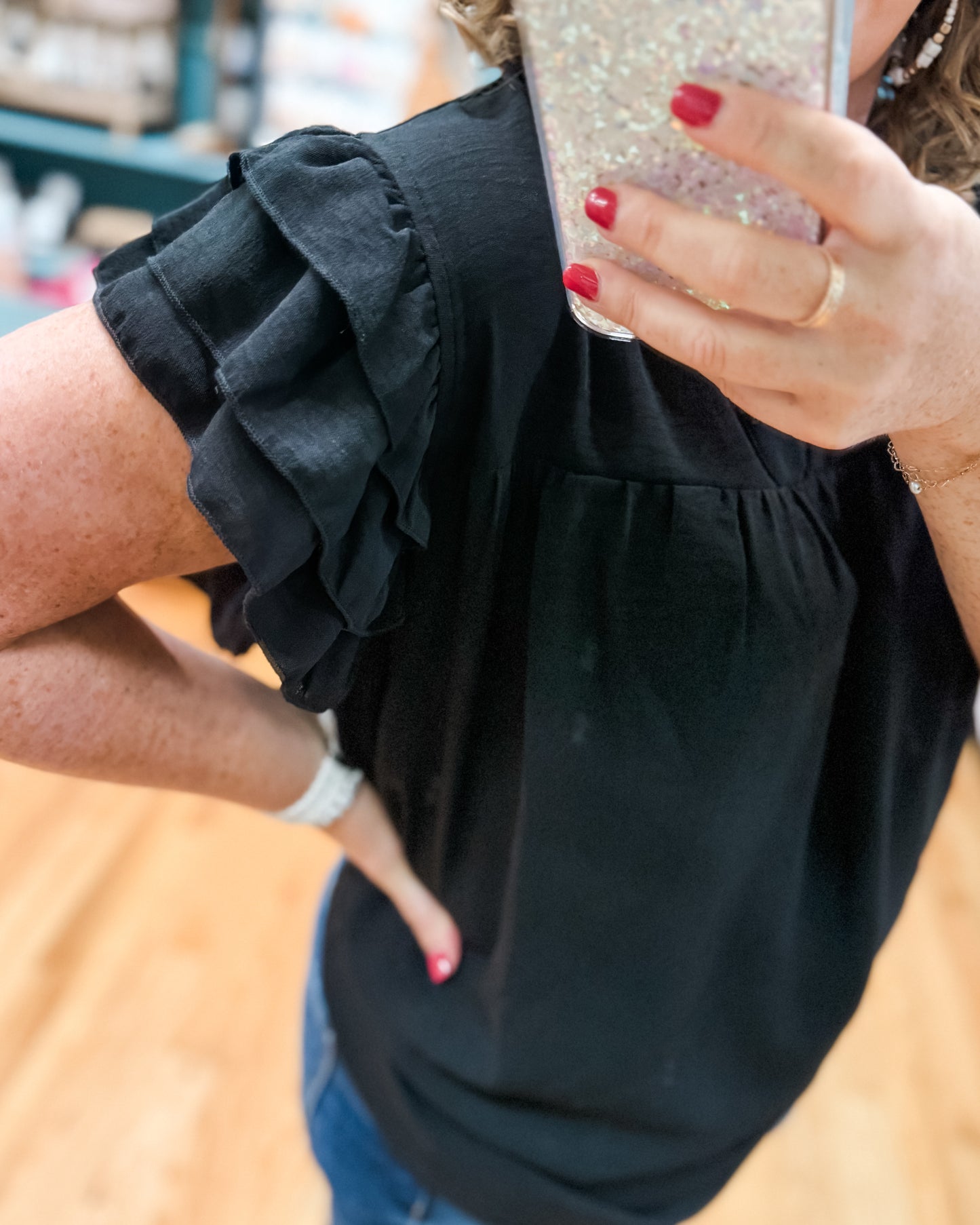 Person wearing a black top with ruffled shoulders, holding a glittery phone case.