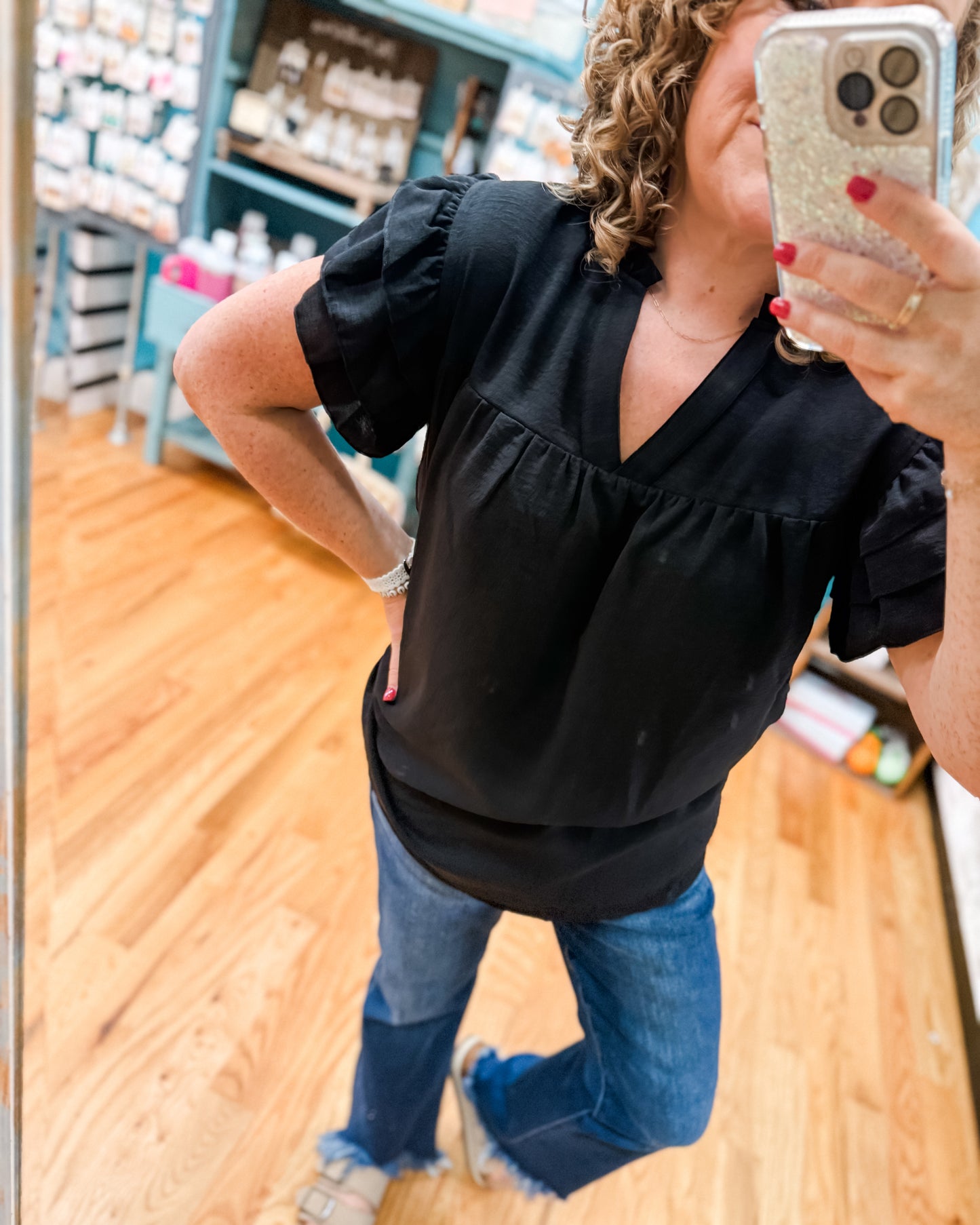 Person taking a mirror selfie wearing a black top and blue jeans in a store.