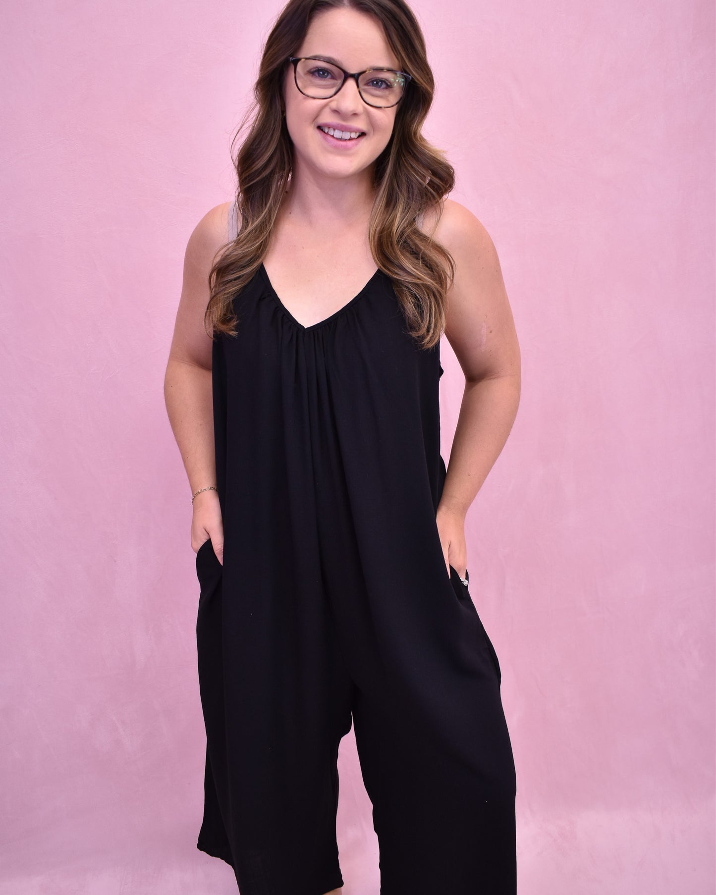 Woman wearing a black sleeveless jumpsuit against a pink background