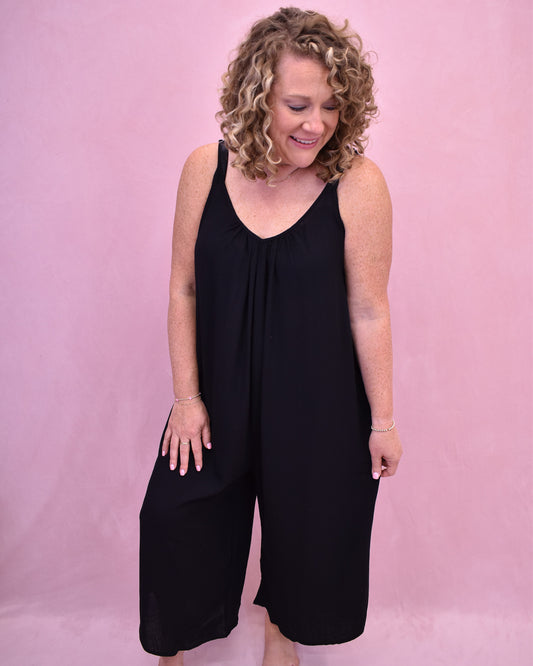Woman wearing a black jumpsuit against a pink background