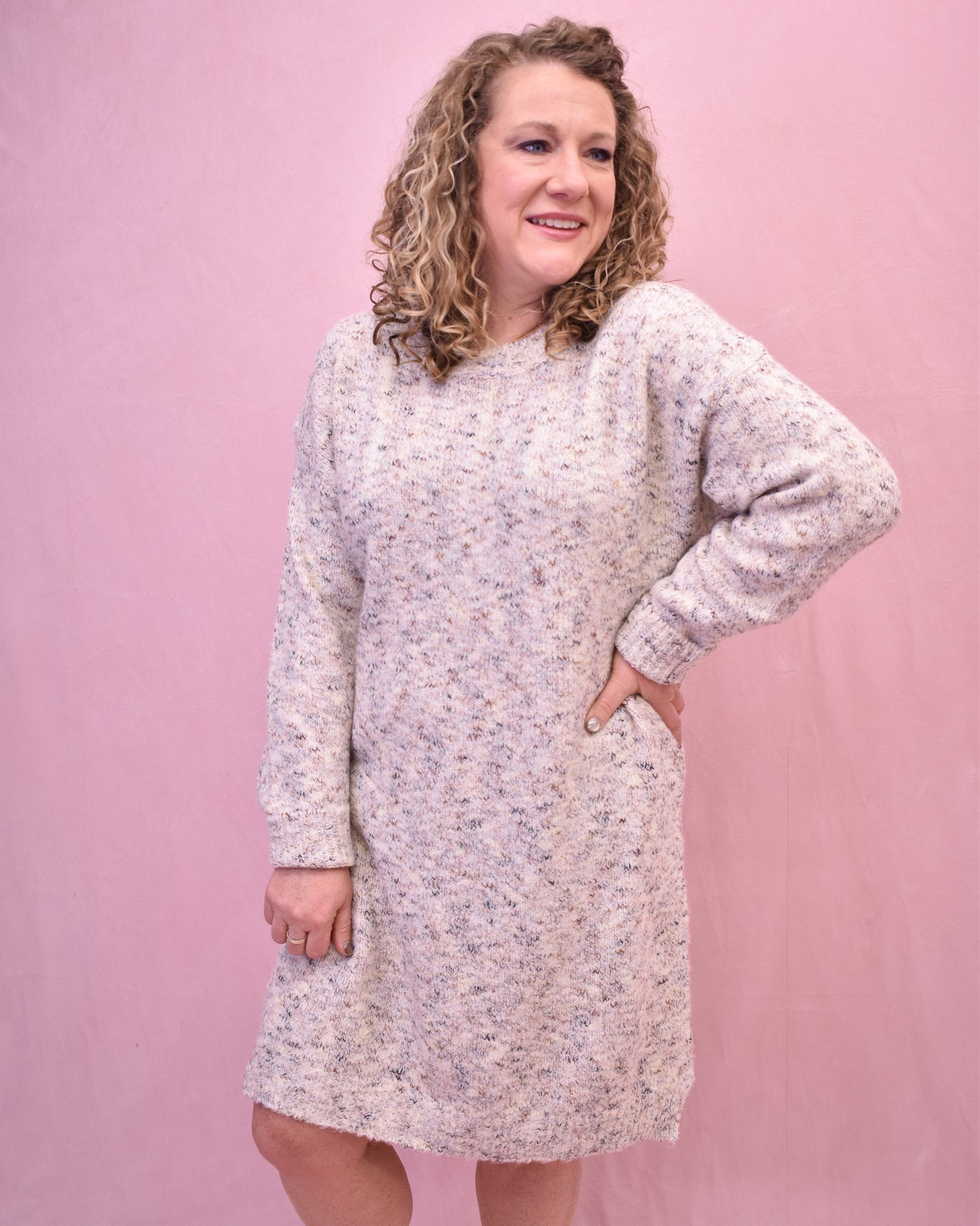 Woman wearing a light-colored sweater dress against a pink background