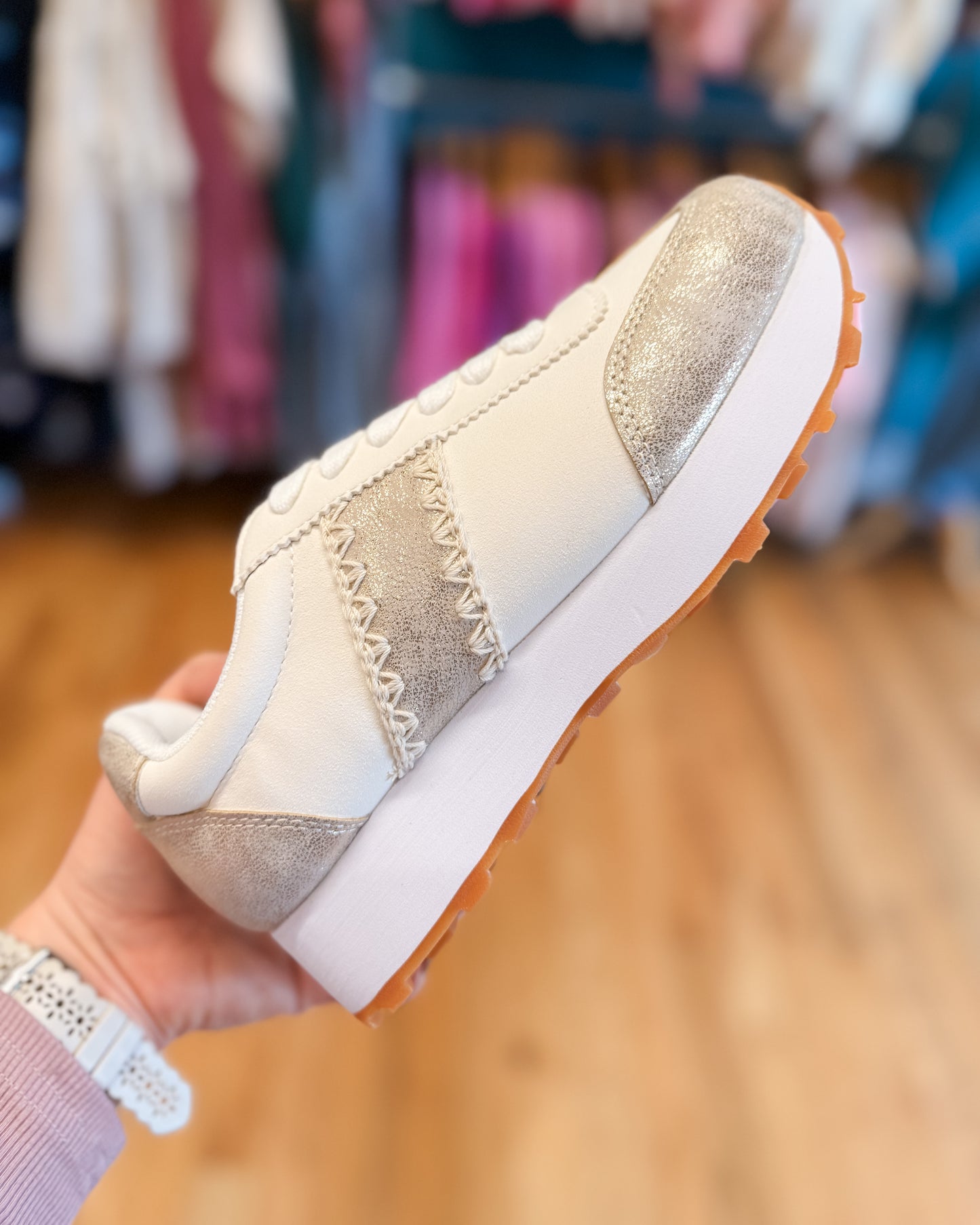 Beige sneaker with white sole held in a hand against a blurred store background