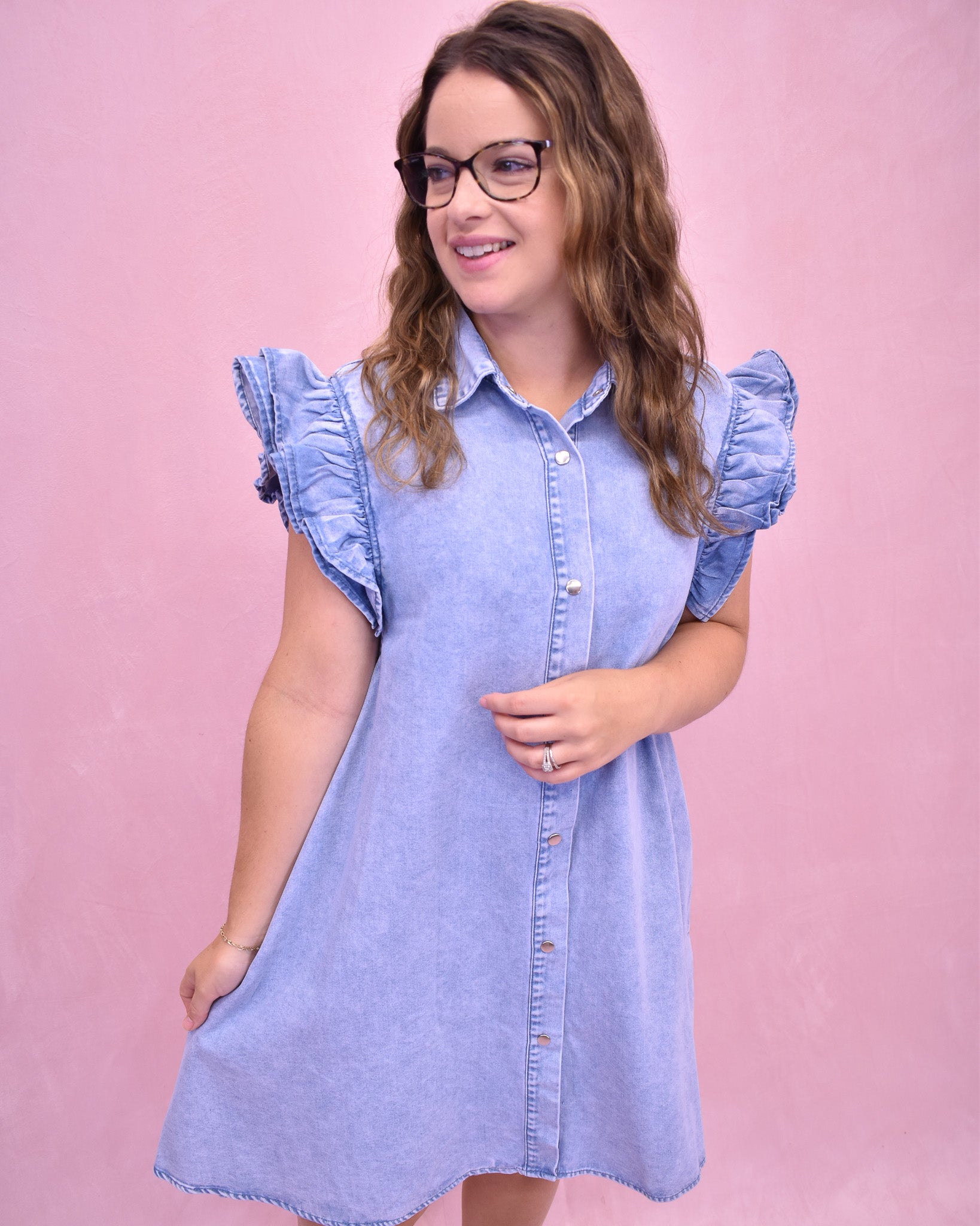 Woman wearing a light blue denim dress against a pink background