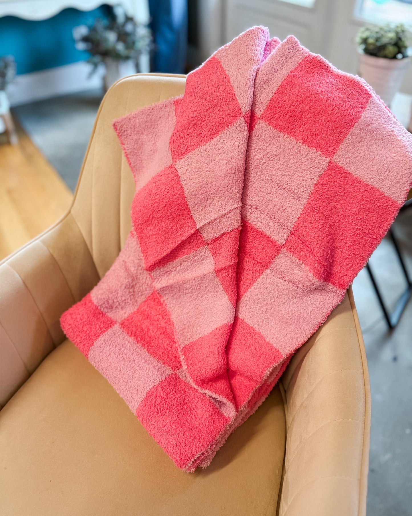 Red and pink checkered blanket draped over a beige chair in a home setting.