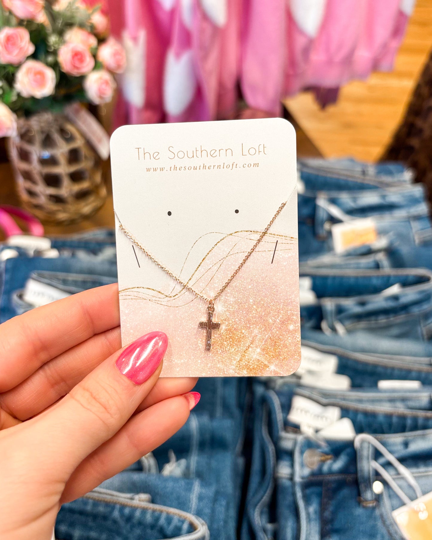 Necklace with cross pendant on a card held over jeans and flowers
