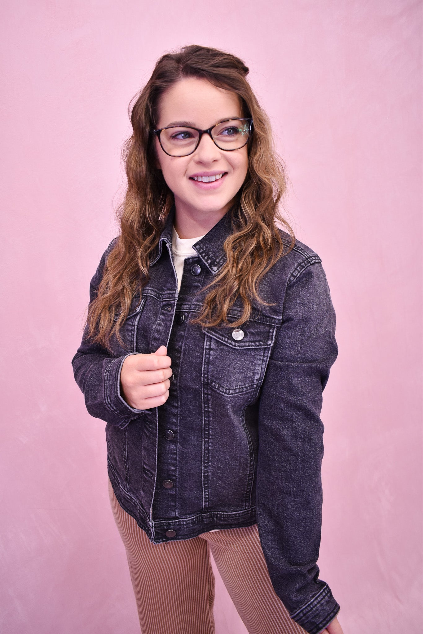 Person wearing a denim jacket against a pink background