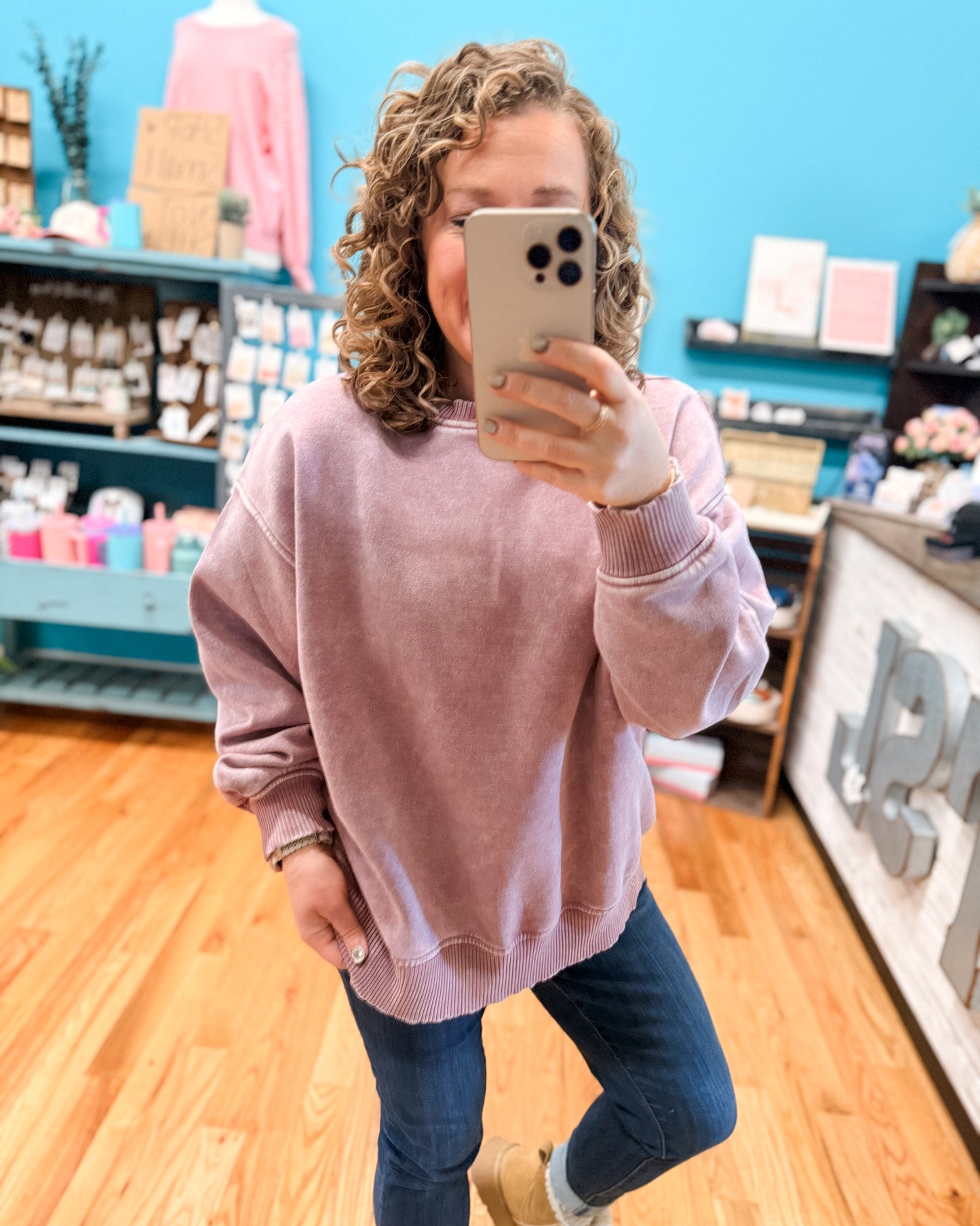 Person wearing a pink sweatshirt and blue jeans taking a selfie in a store.