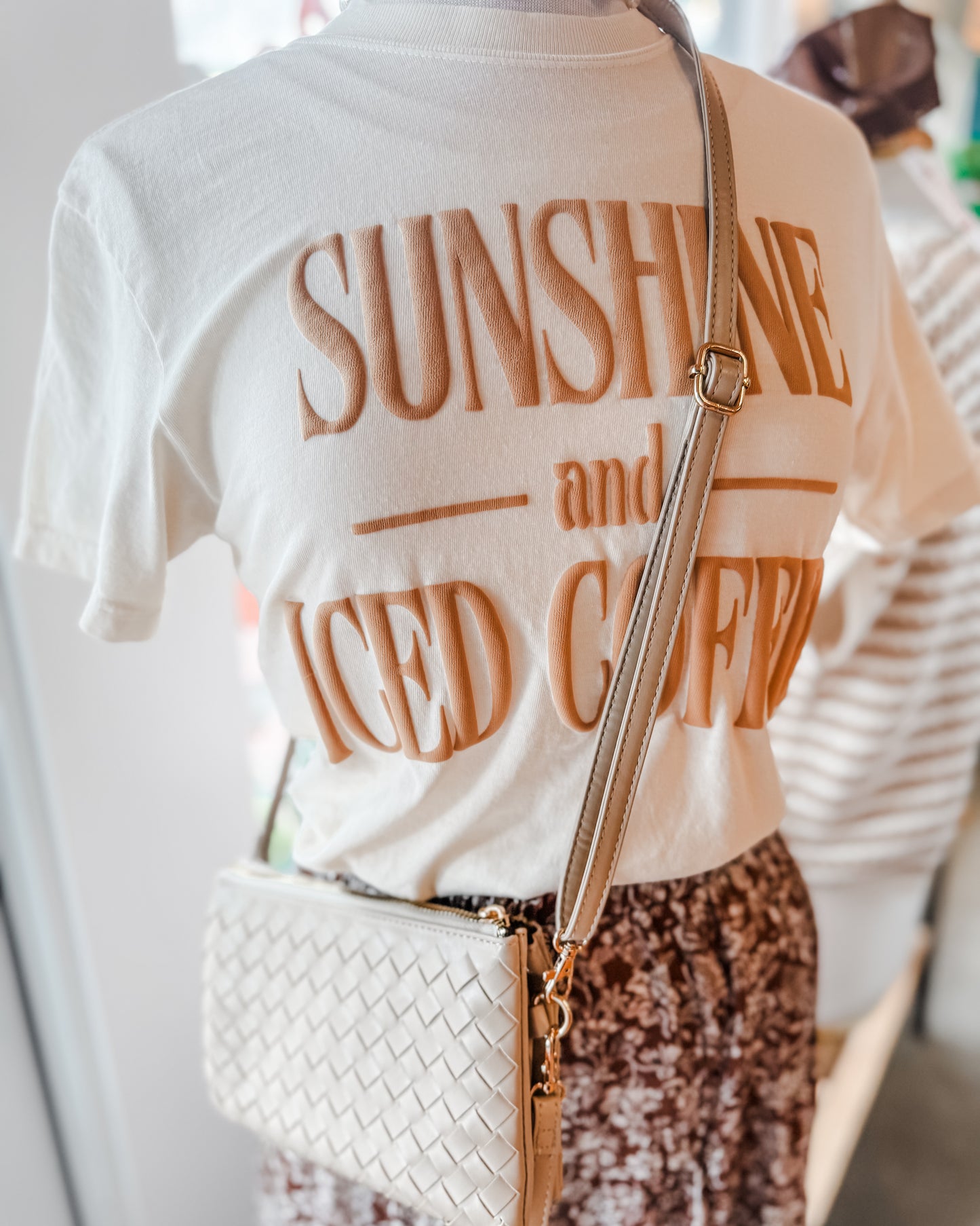 Person wearing a white t-shirt with 'Sunshine and Iced Coffee' text, holding a white handbag.