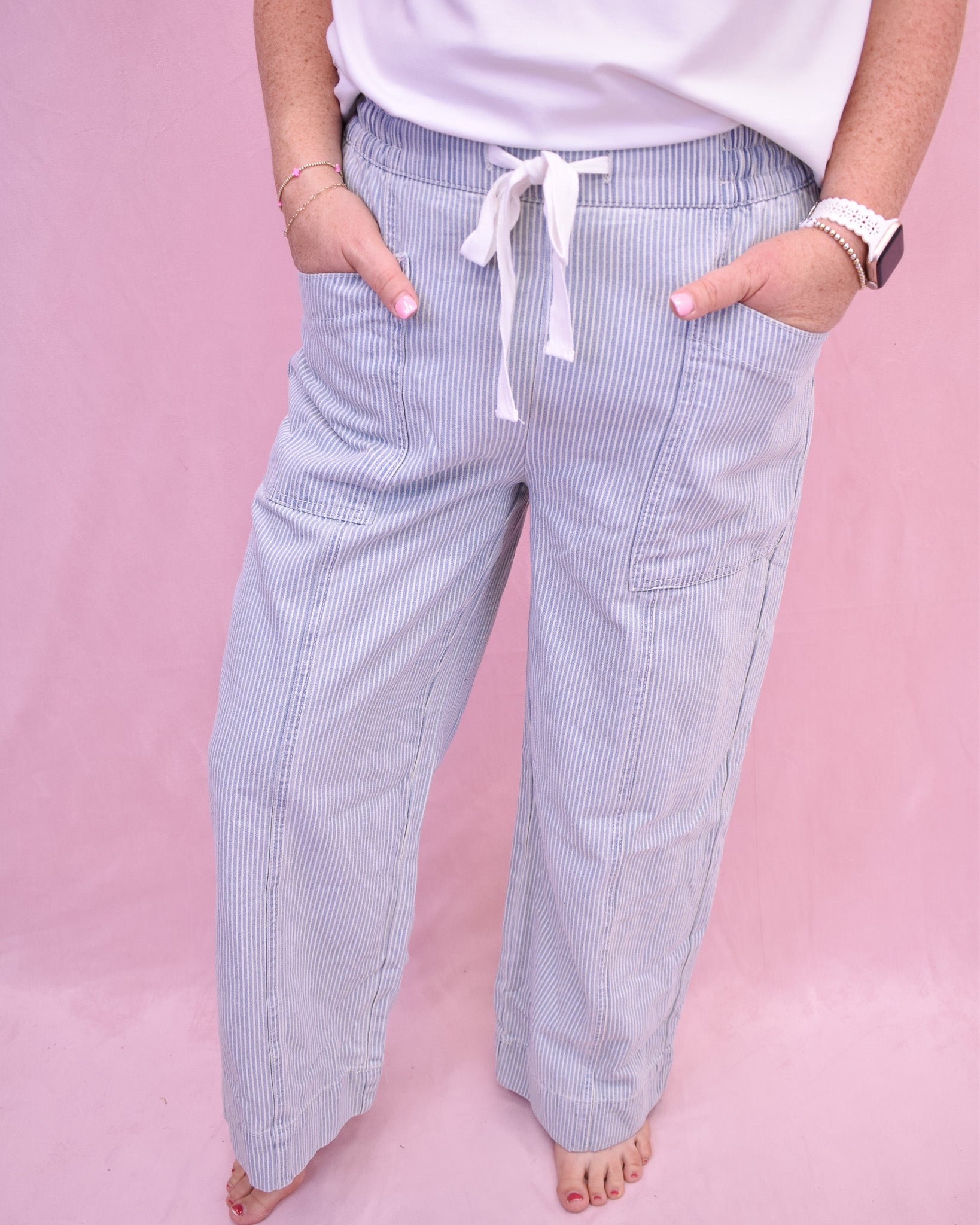 Person wearing blue striped pants with a white top on a pink background
