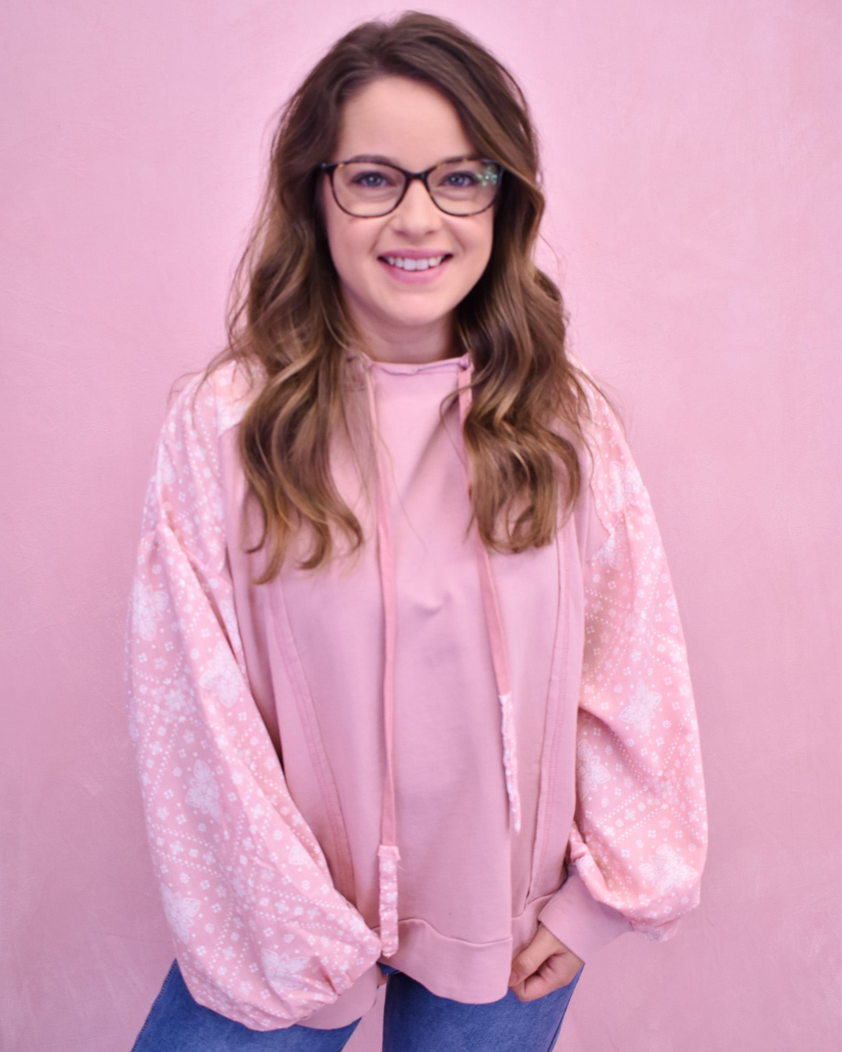 Woman wearing a pink blouse with sheer sleeves against a pink background