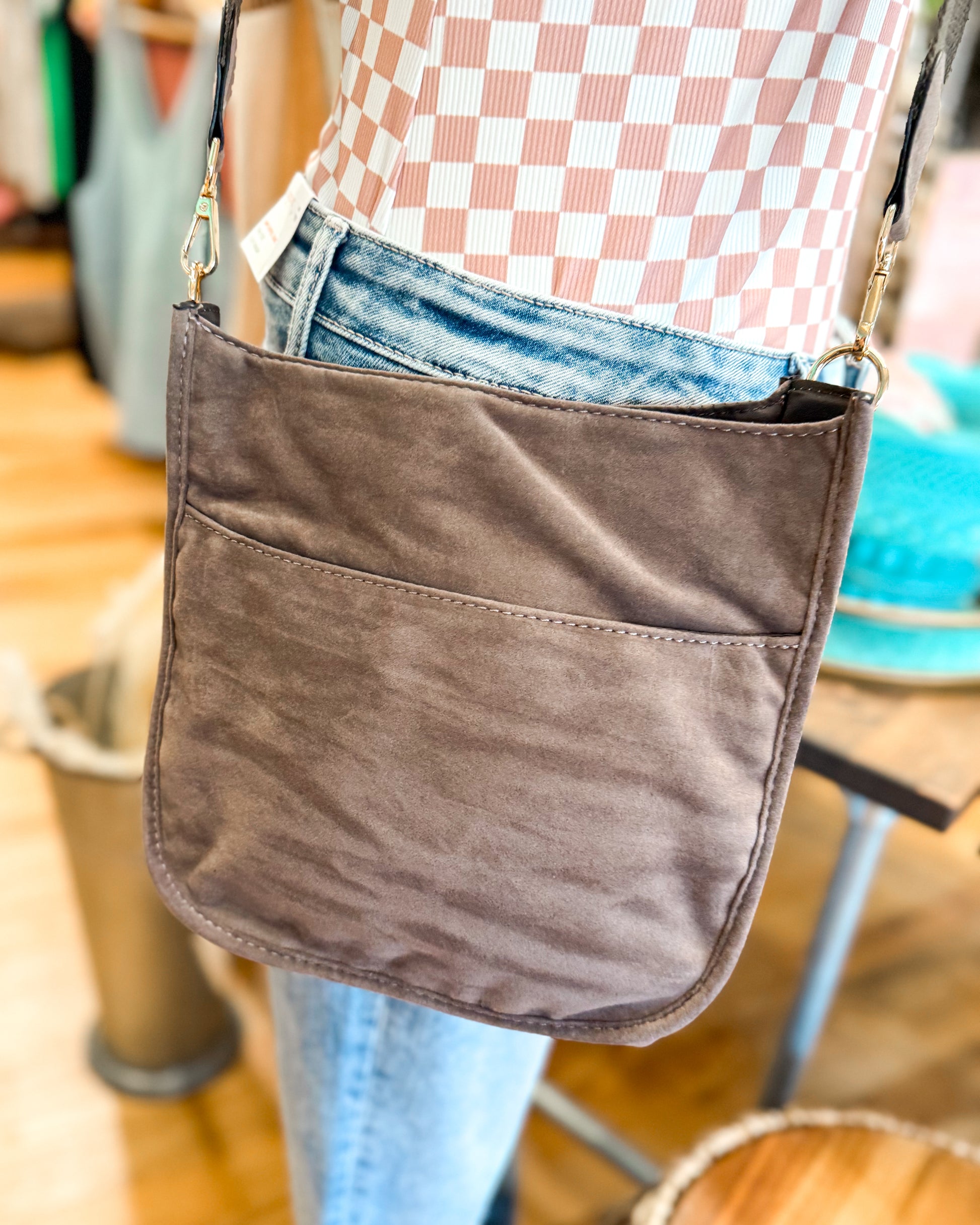 Person wearing a brown crossbody bag with a checkered shirt and jeans in an indoor setting.