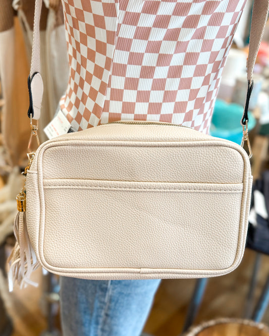 Beige handbag with tassel details worn by a person in a checkered shirt.