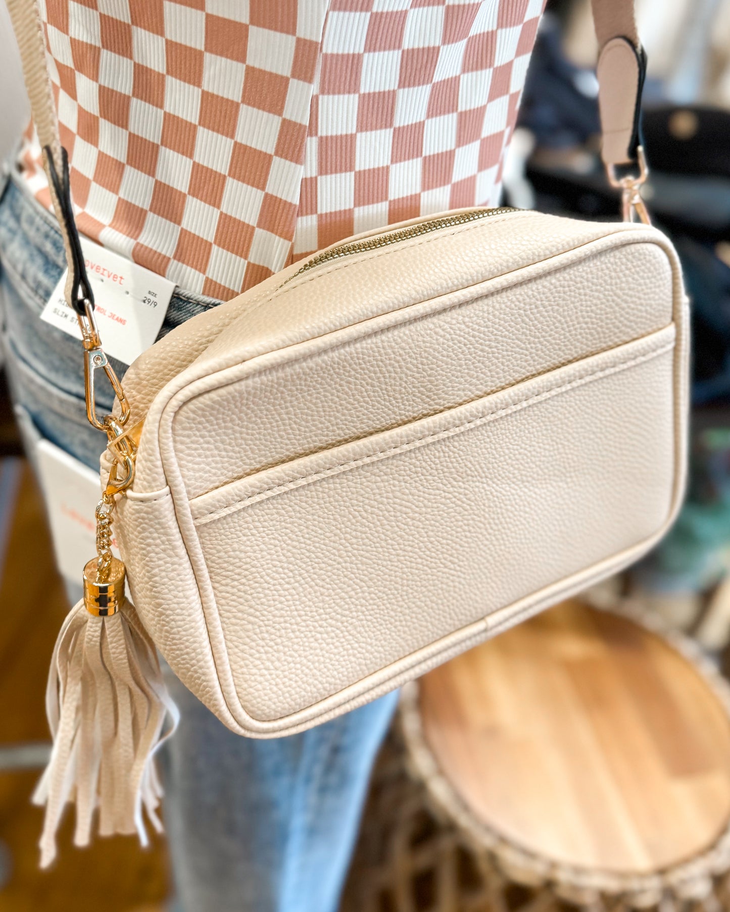 Beige crossbody bag with tassel detail worn by a person in a checkered shirt.