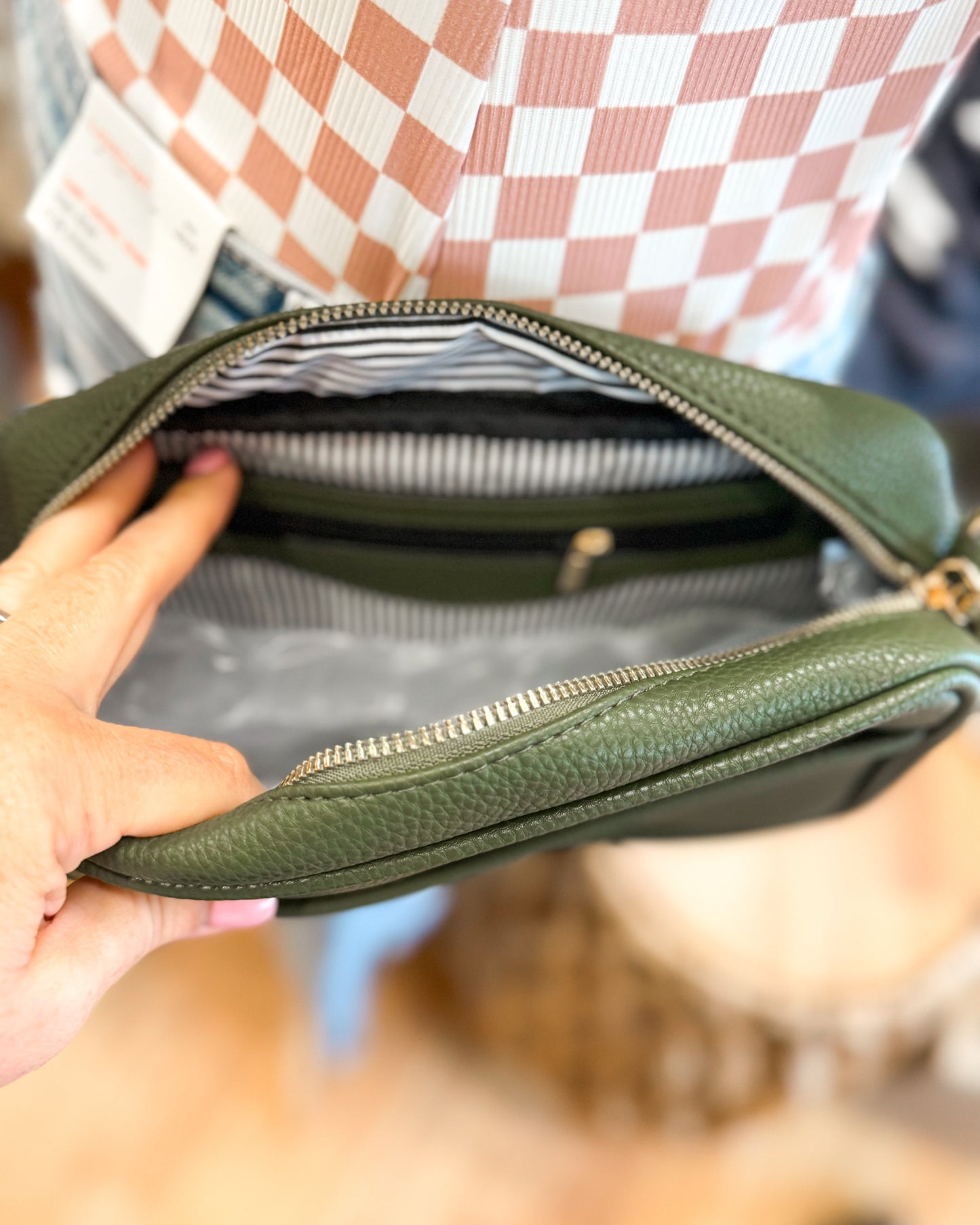 Green leather bag held by a person with a checkered shirt in the background