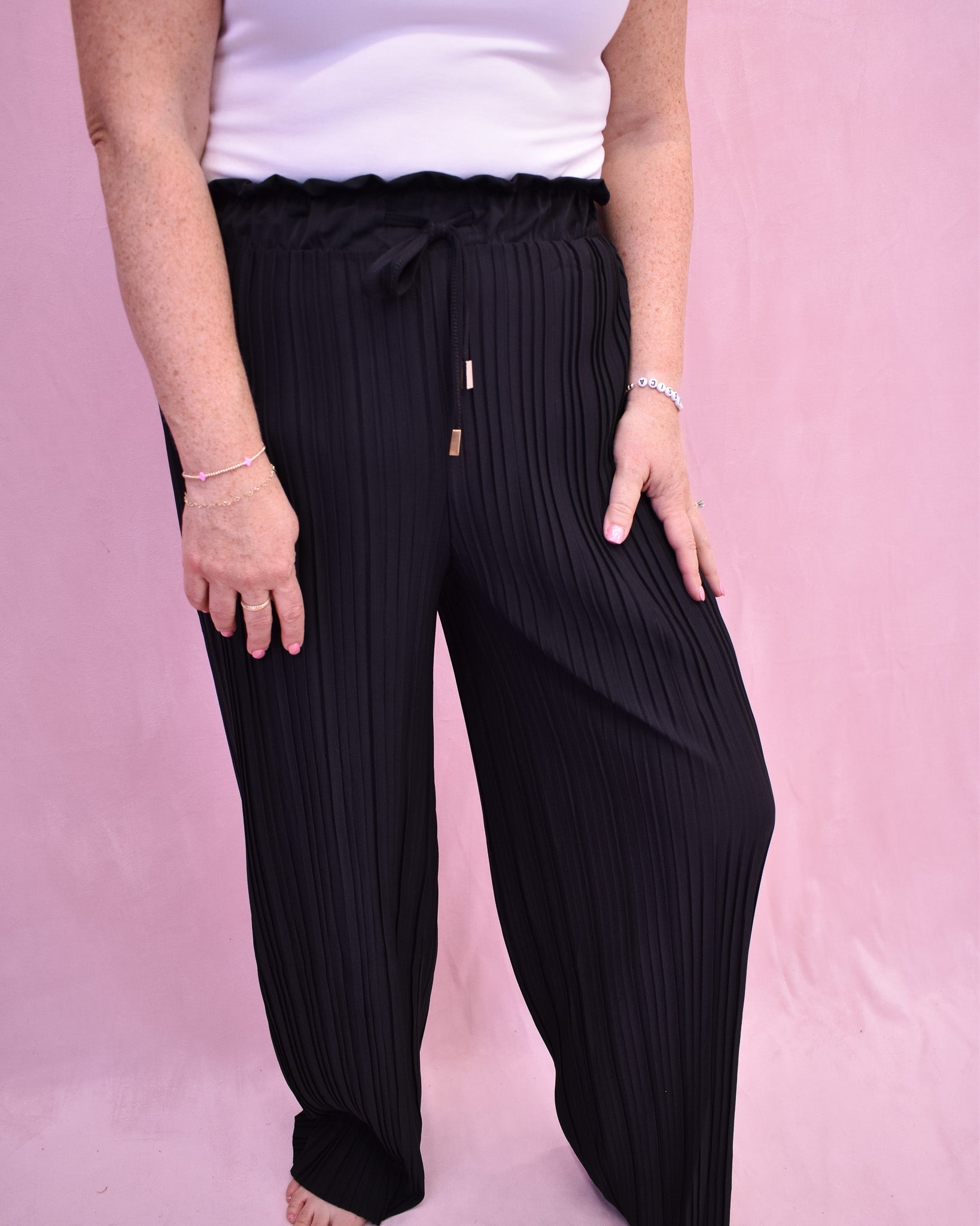 Person wearing black pleated pants on a pink background