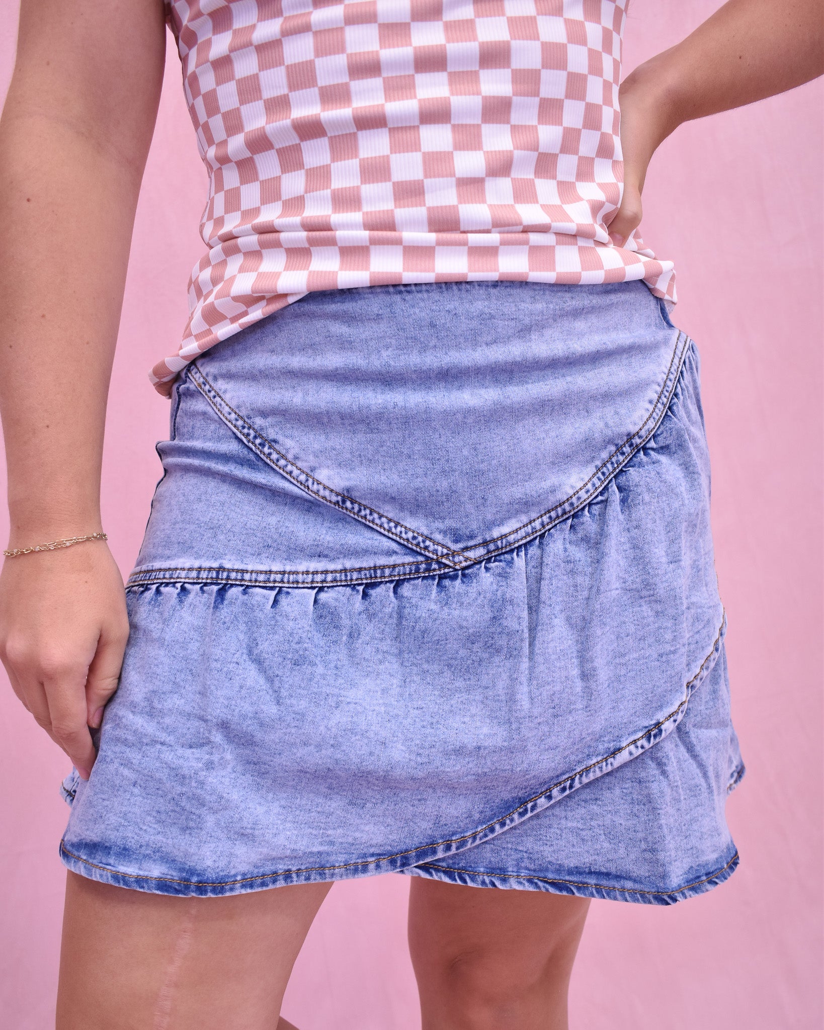Person wearing a denim skirt and checkered top on a pink background
