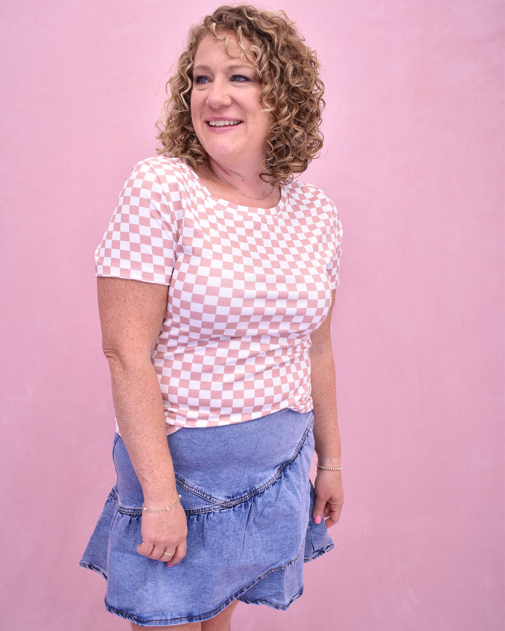Woman wearing a pink checkered top and denim skirt against a pink background