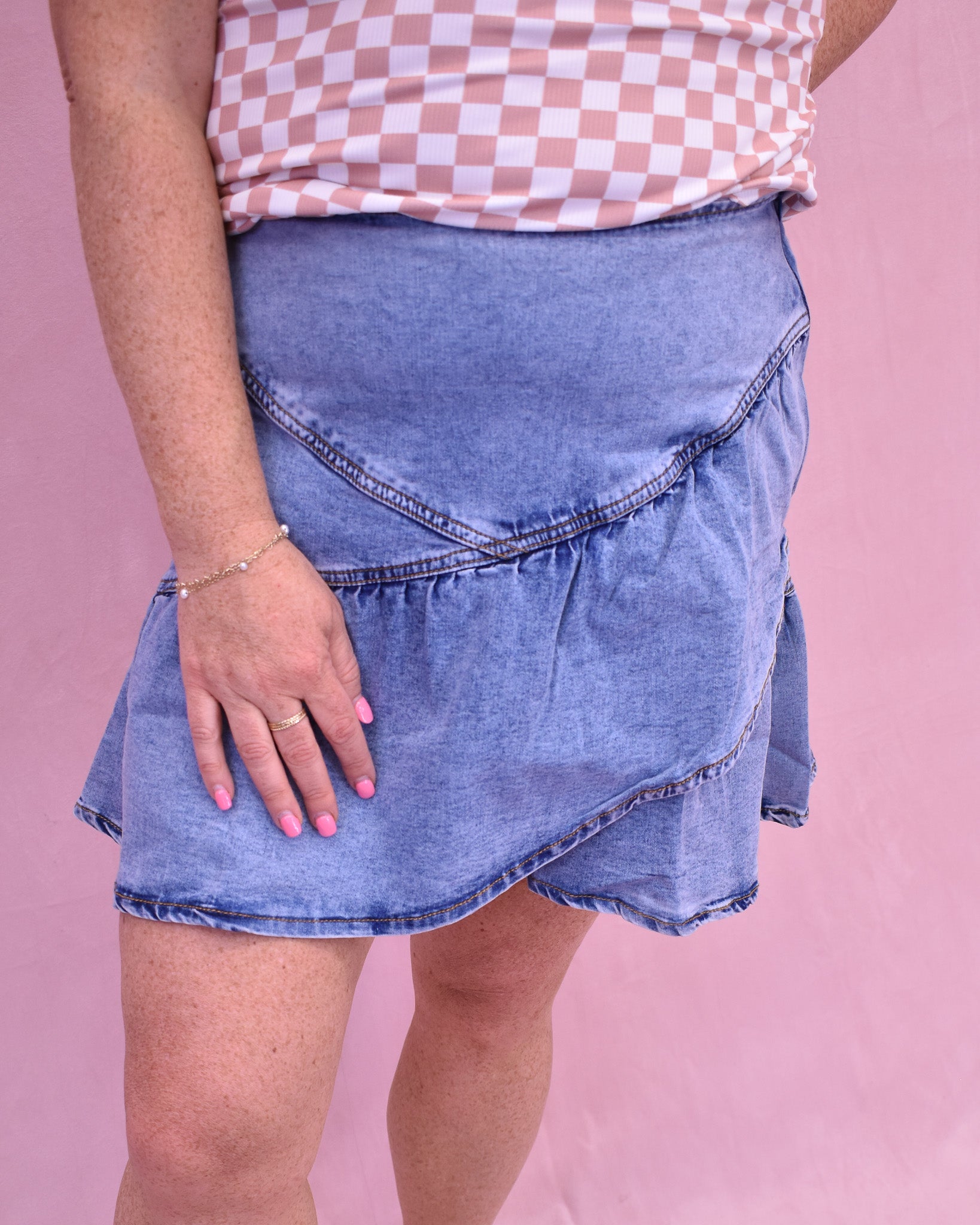 Person wearing a blue denim skirt and checkered top on a pink background