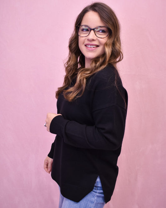 Woman wearing a black sweater and glasses against a pink background
