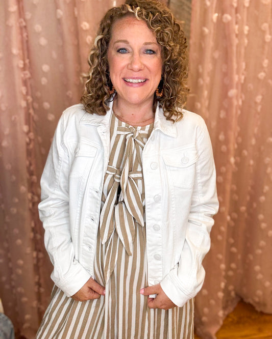 Woman wearing a white jacket over a striped dress with a beige curtain background