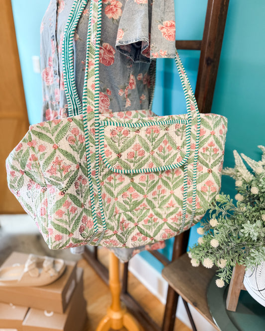 Floral patterned bag on a mannequin against a blue wall with a plant in the foreground.
