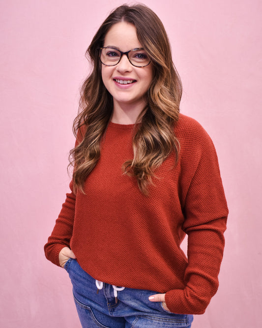Woman wearing a red sweater and glasses against a pink background