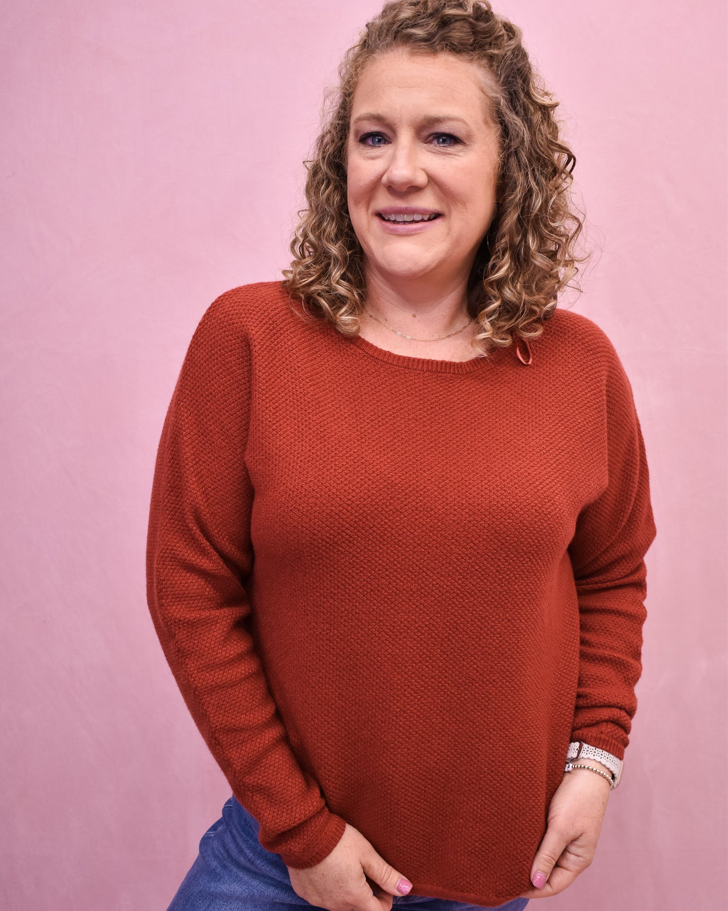 Woman wearing a rust-colored sweater against a pink background