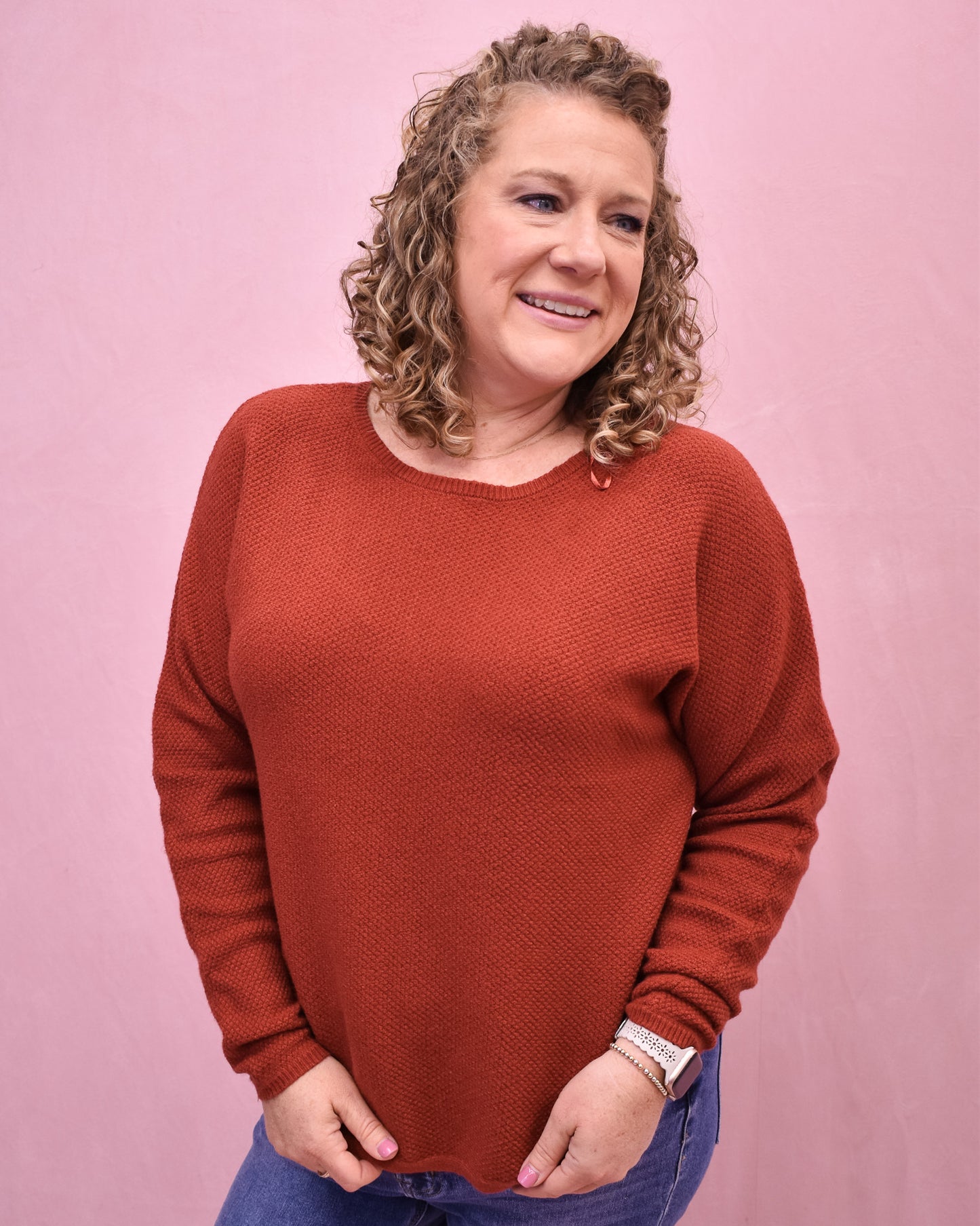 Woman wearing a rust-colored sweater against a pink background