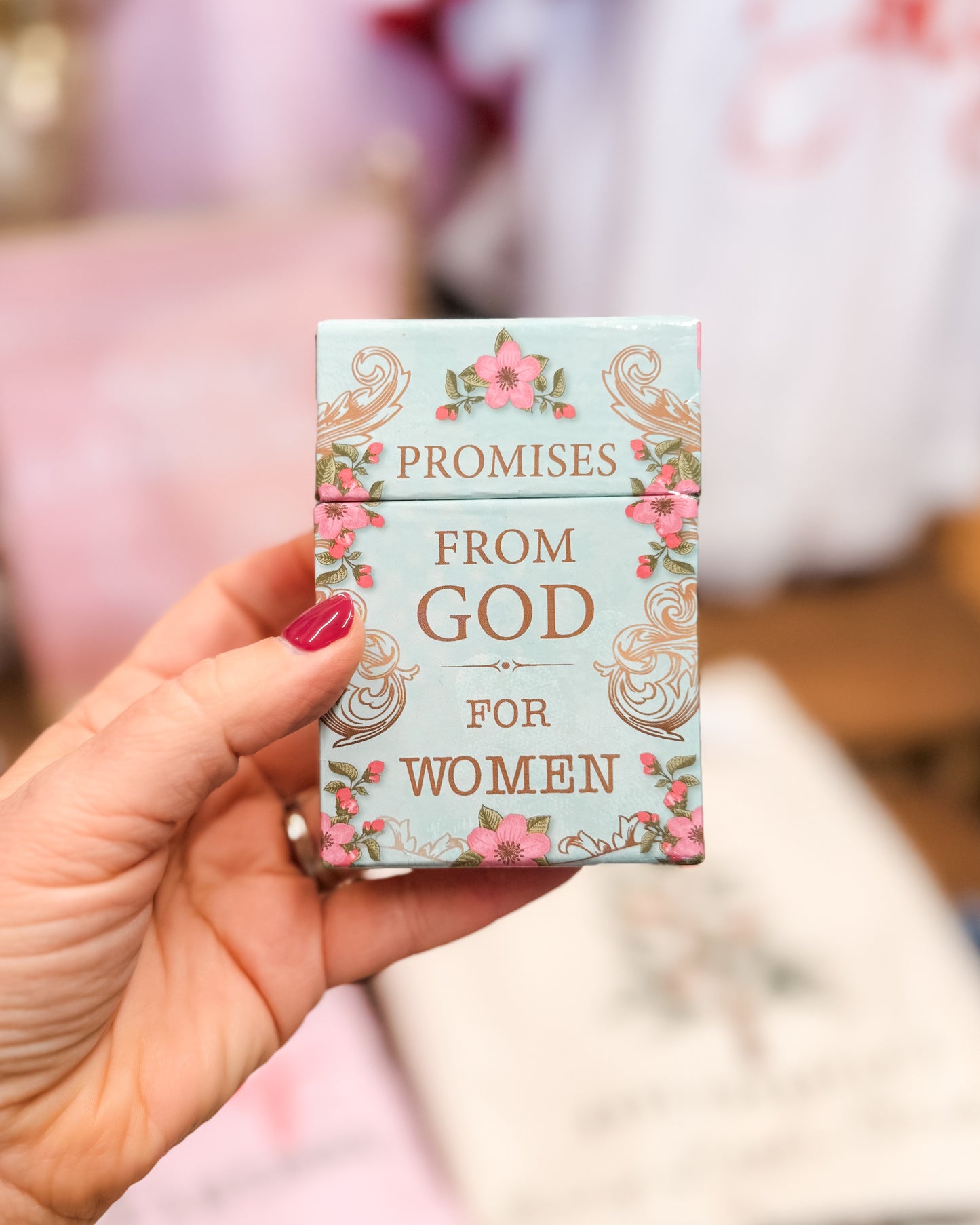 Hand holding a book titled 'Promises from God for Women' with floral design on a blurred background