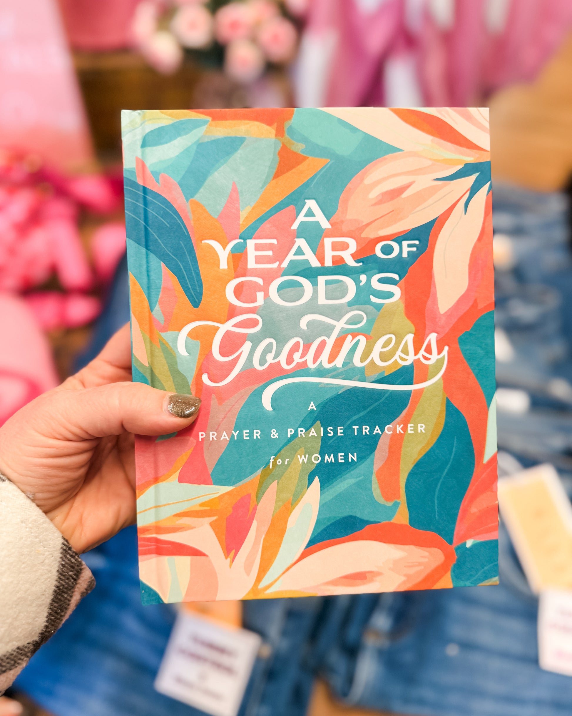 Colorful book titled 'A Year of God's Goodness' held by a person with a blurred background.