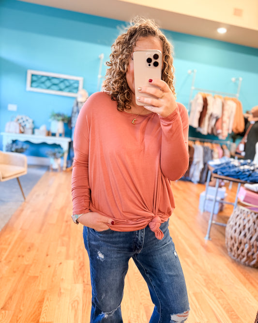 Person taking a mirror selfie wearing a peach long-sleeve top and jeans in a store.