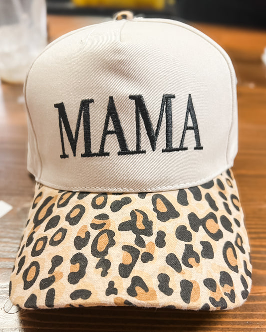 Beige cap with 'MAMA' text and leopard print brim on a wooden surface