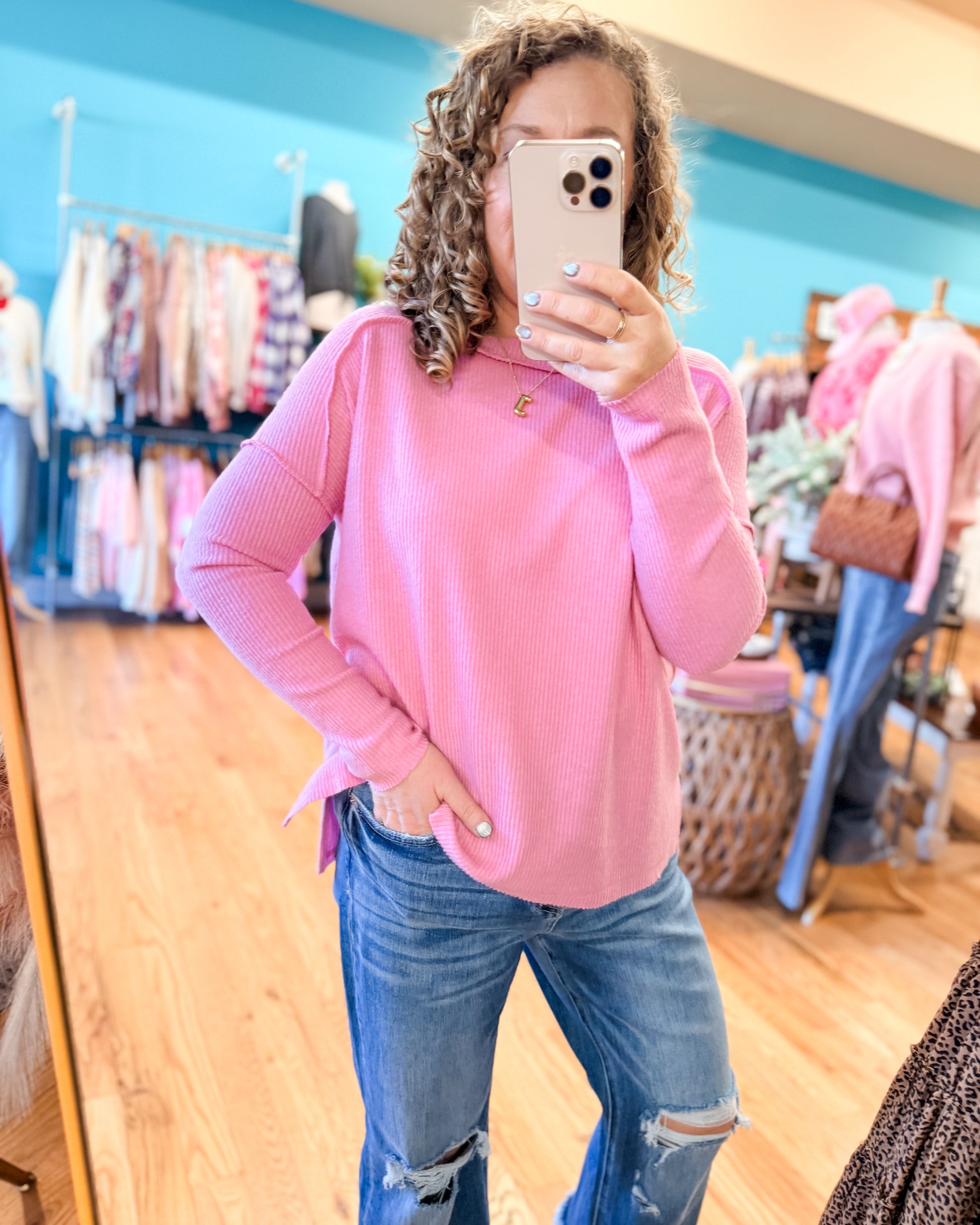 Person wearing a pink sweater and blue jeans taking a mirror selfie in a store.