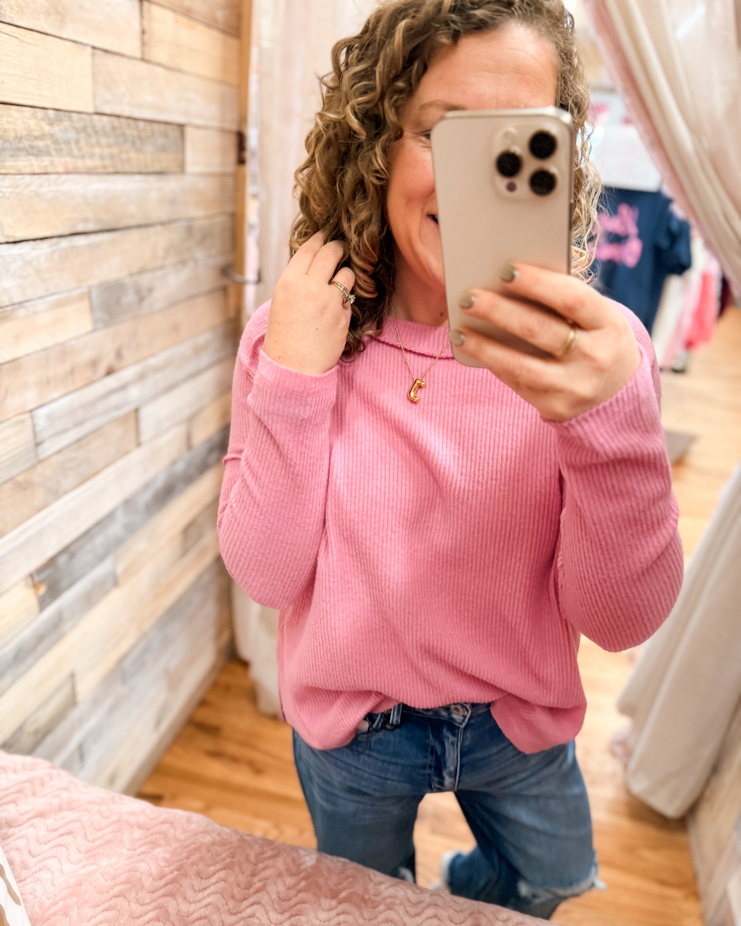 Person wearing a pink sweater and blue jeans taking a mirror selfie.