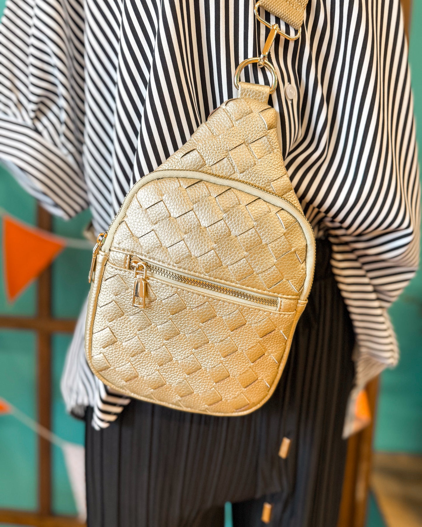 Gold woven backpack worn by a person with a striped shirt and pleated skirt.