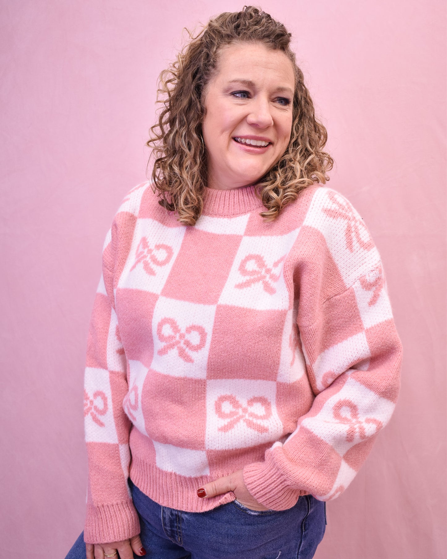 Person wearing a pink and white checkered sweater with bow patterns against a pink background
