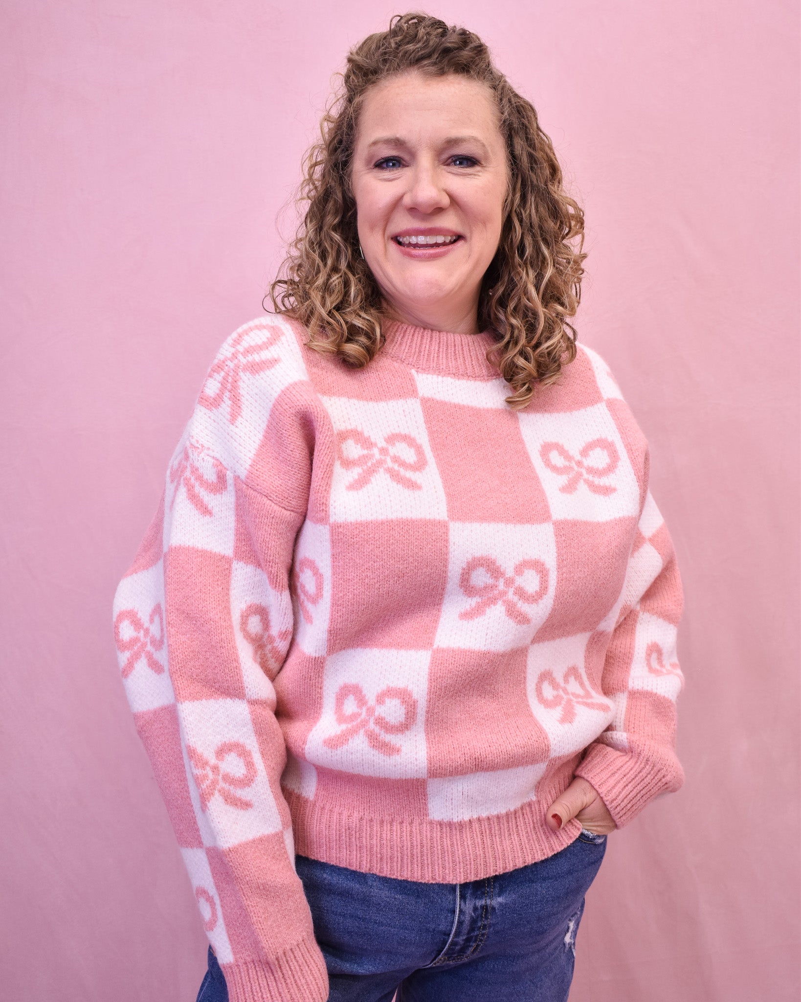 Person wearing a pink and white checkered sweater with bow patterns against a pink background