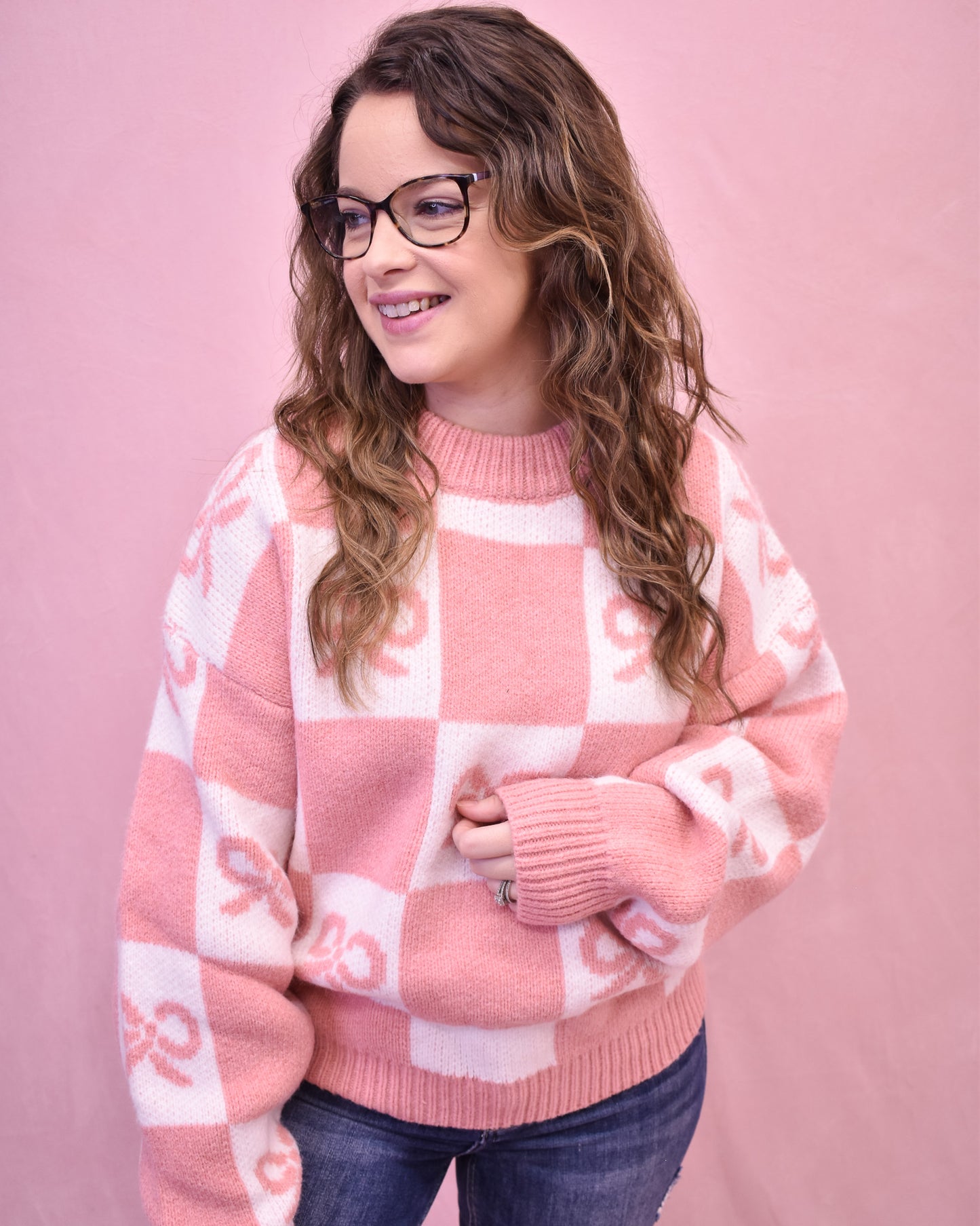 Woman wearing a pink and white checkered sweater against a pink background