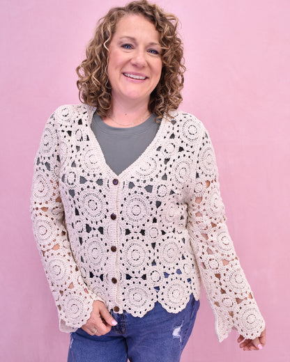 Woman wearing a white crochet cardigan against a pink background