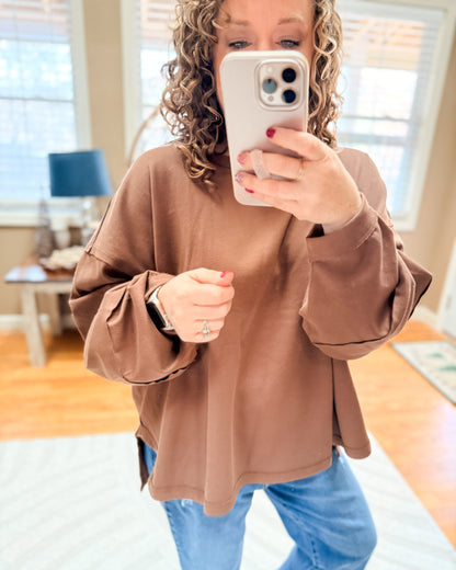 Person wearing a brown oversized sweater and blue jeans taking a mirror selfie.