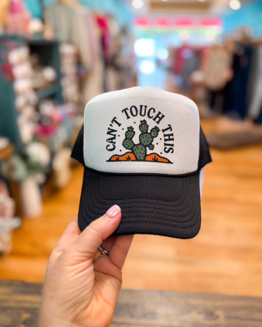 Black and white cap with 'Can't Touch This' cactus design held in a store setting