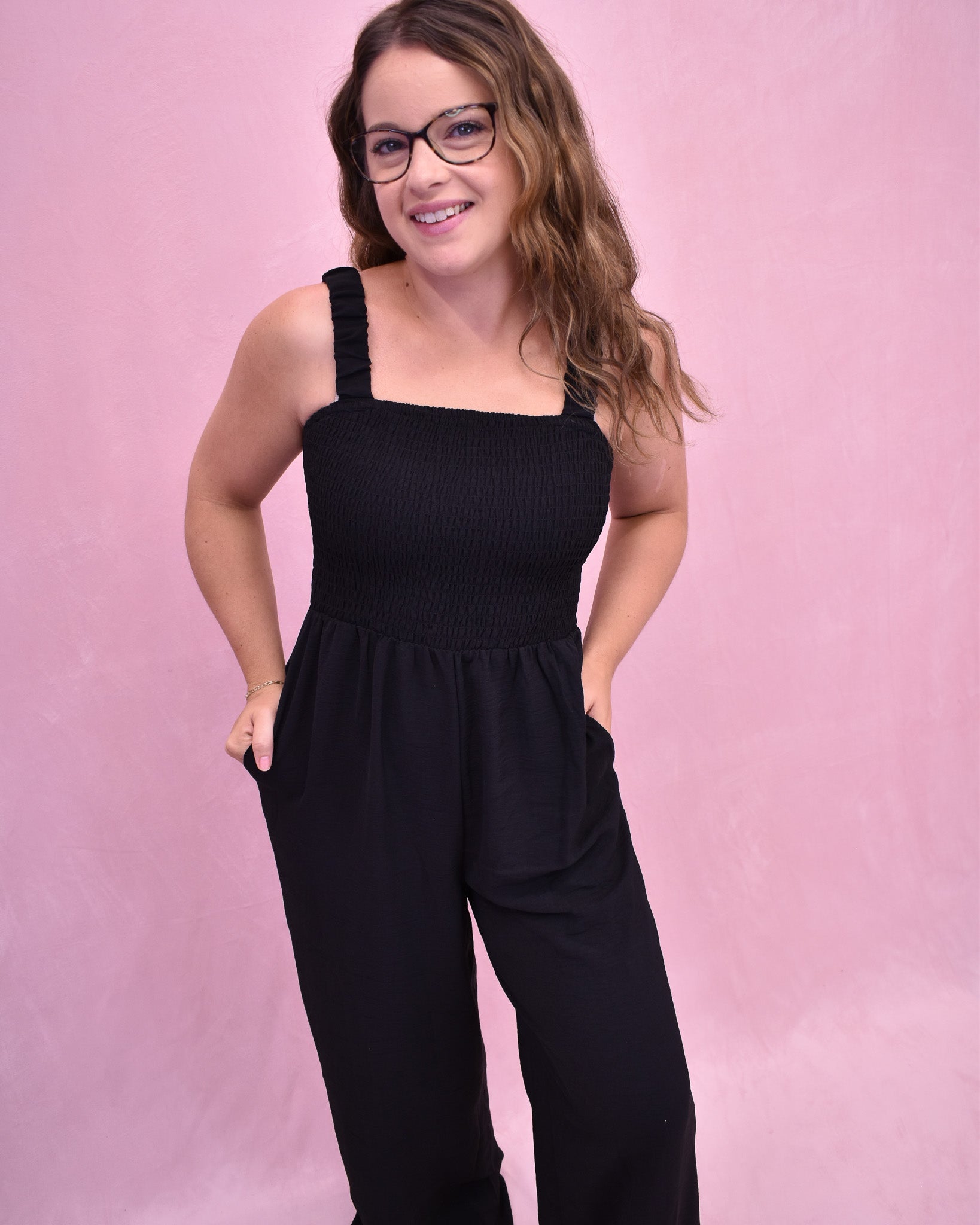Woman wearing a black jumpsuit against a pink background